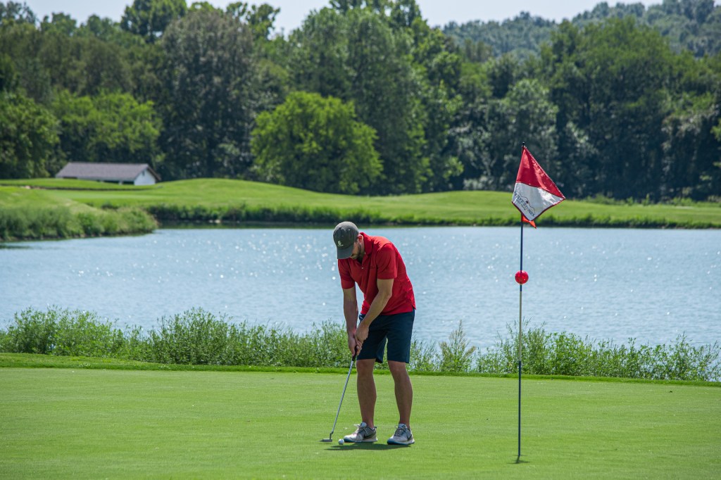 golfer taking a swing on golf course hole with red and white flag
